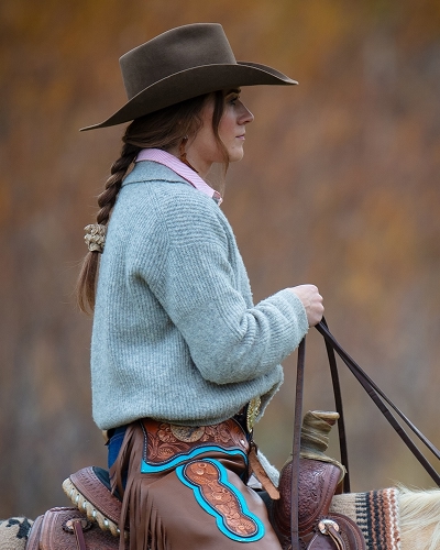 Alle Carter riding horseback in a cowboy hat and jean jacket. She's looking to the distance with a thoughtful look on her face.